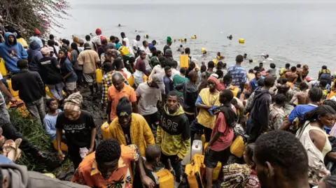 AFP Many people in a crowd carrying their jerrycans as they gather to collect water amid ongoing water shortages at the shore of Lake Kivu in Goma 