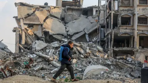 Getty Images Boy walking past damaged buildings in Khan Yunis, Gaza on 11 January 2025. 