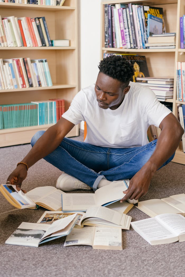 Young man studying books while sitting on a library floor.